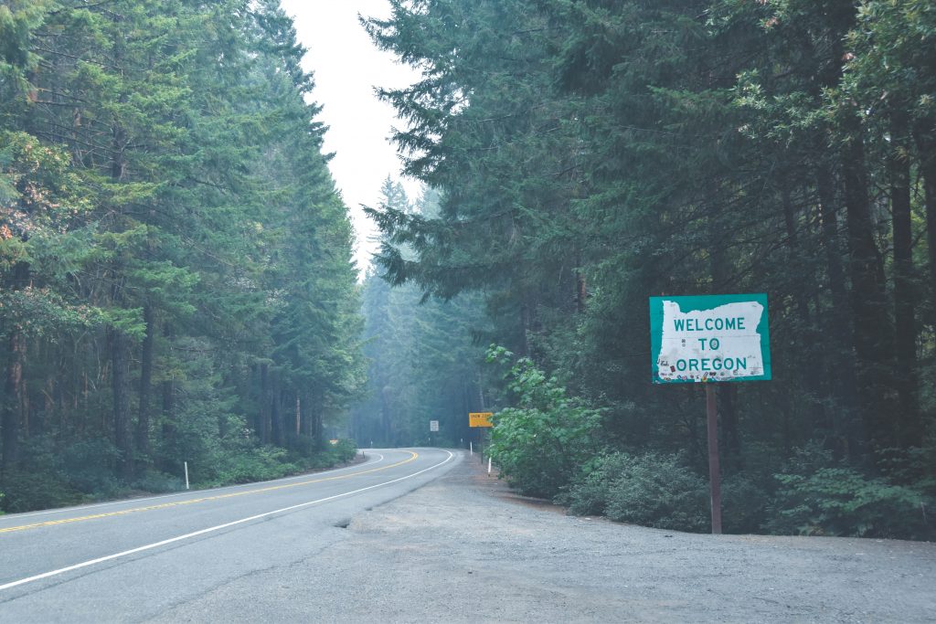 Image of a forested road at the Oregon border featuring a Welcome to Oregon sign.