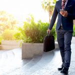 Businessman walking on the stairs and using smartphone outdoors