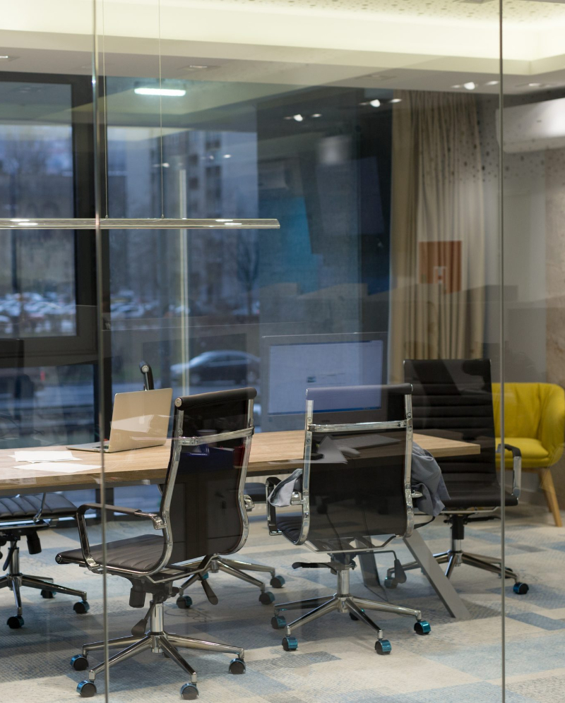 Empty conference room with glass walls, a desk, and some chairs.