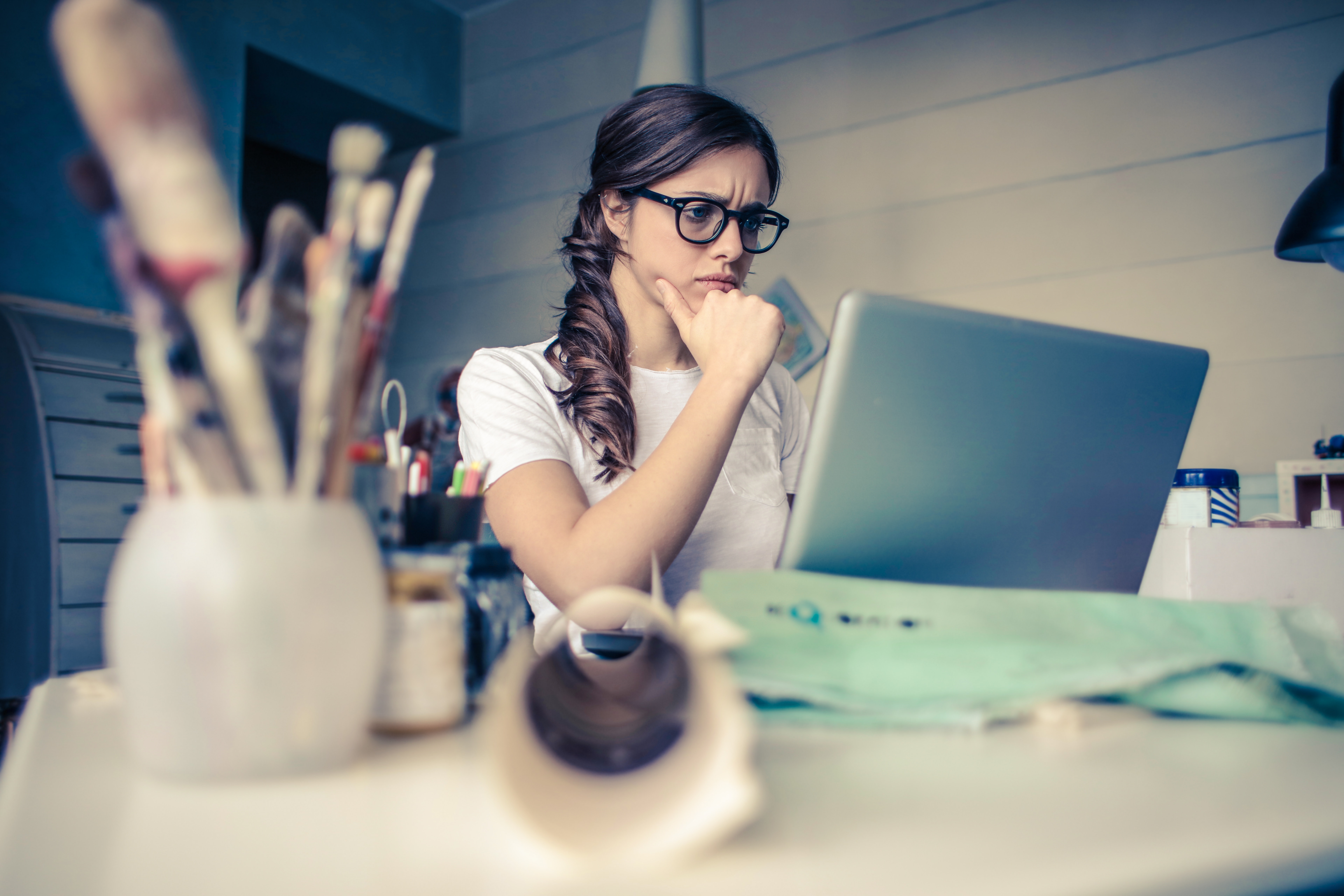 A young women in front of her lap top with art supplies in the foreground.